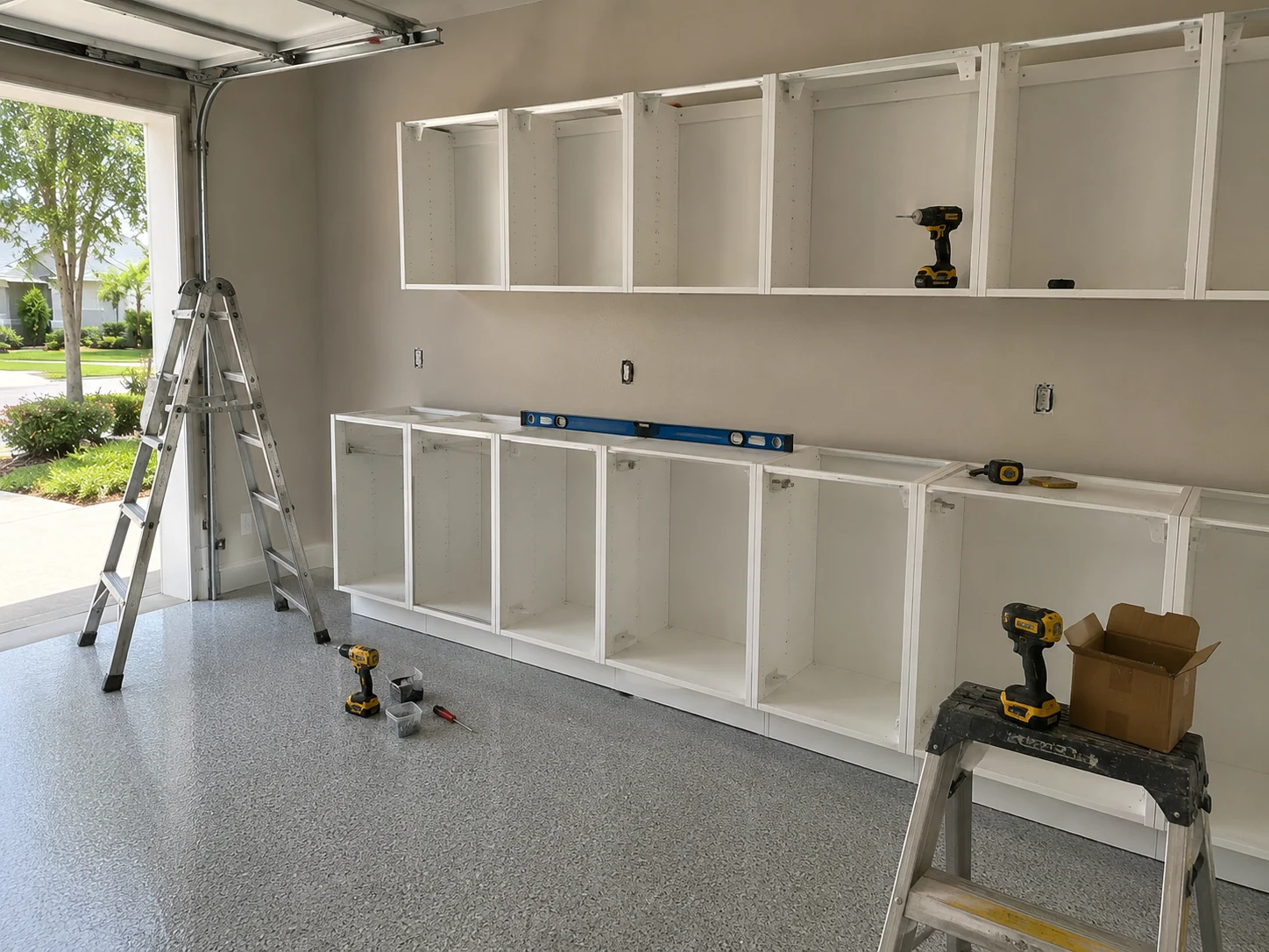 Garage under construction with cabinet boxes being set along the wall and electrical outlet boxes roughed in, garage door open to the street