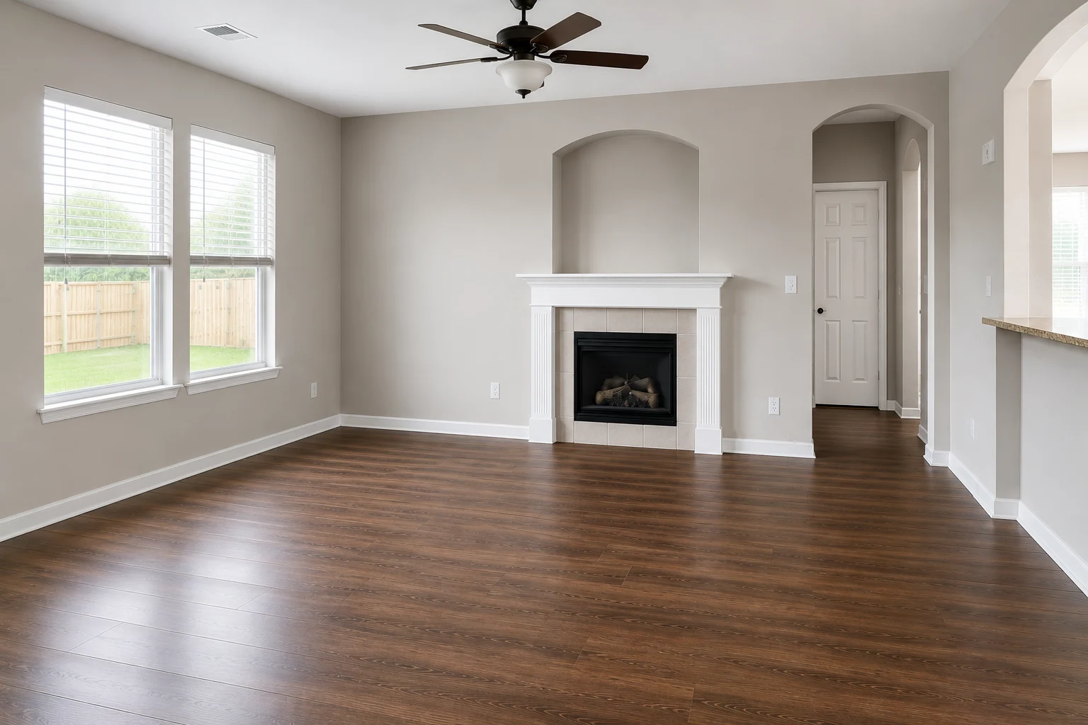 Living room finished in a warm neutral wall colour with white trim and baseboards, natural light from two windows and a dark wood-look floor